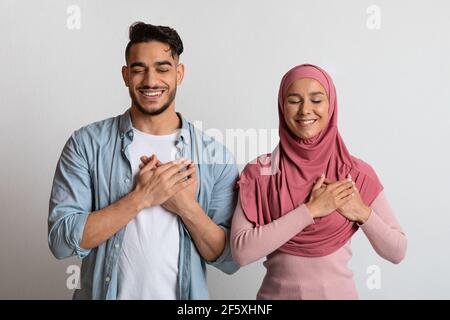 Thankful Muslim Couple Keeping Hands On Chest Expressing Gratitude Together Stock Photo