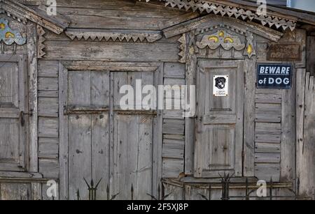 Old dilapidated wooden facade of the house with carved platbands, curly wall elements and metal bars, with a sign Beware of dog. Stock Photo
