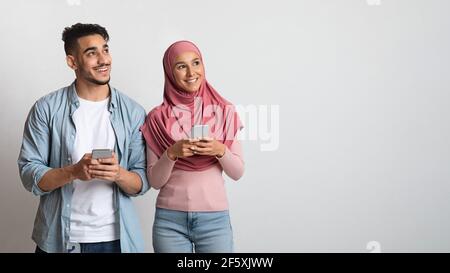 Happy Muslim Couple With Smartphones In Hands Looking Aside At Copy Space Stock Photo