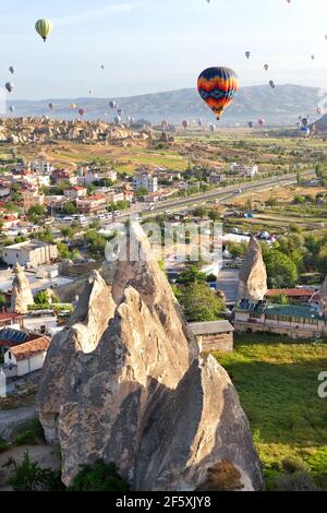 Sunny landscape of Goreme city with dozens of balloons flying in the sky of Cappadocia at sunrise in central Turkey. Stock Photo