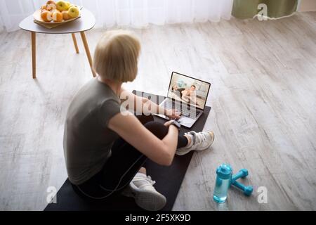 Senior woman watching online video sports tutorial on laptop, taking break from her domestic training Stock Photo