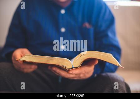 Elderly man sitting on the couch and reading Bible Stock Photo