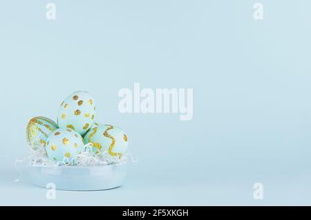 Blue easter eggs with gold glitter design on bowl on blue background, copy space. Stock Photo