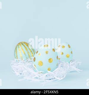 Elegant easter eggs with gold dots in white nest on blue background, square. Stock Photo