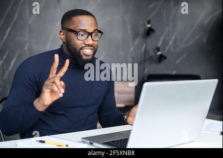 Concept of video meeting using modern technology. African man showing victory sign, using app on PC for video connect with family or friends in another country. Distant connection concept Stock Photo
