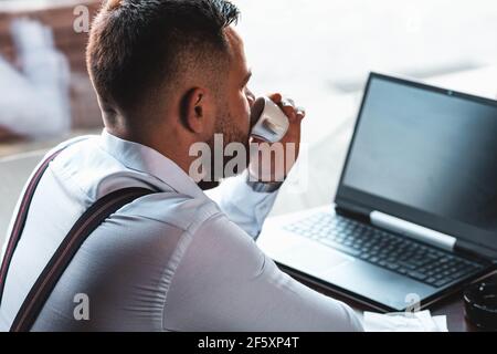 Young businessman working on a laptop in a cafe, drinking espresso coffee Stock Photo