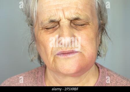 Depressed mature woman isolated on grey studio background touch cheek suffering from tooth pain Stock Photo