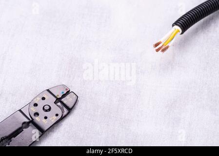 Wire stripper pliers and exposed electrical cable on the electrician's desk. Stock Photo
