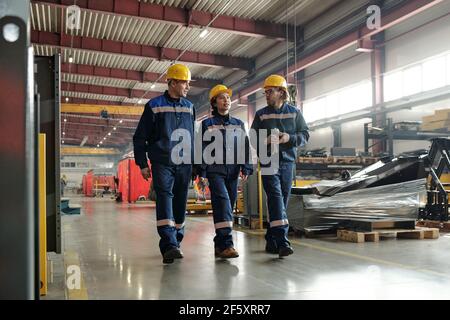 Group of workers or engineers of contemporary industrial plant moving along large workshop with equipment and having conversation Stock Photo