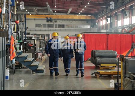 Group of workers or engineers of contemporary factory moving along large workshop with industrial equipment and having conversation Stock Photo