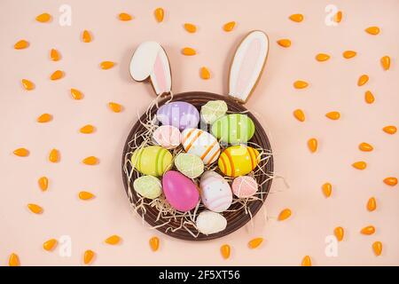 Gingerbread easter bunny ears and painted easter eggs on plate and candy in the form of carrots on a pink background. Sweets for celebrating Easter. Stock Photo