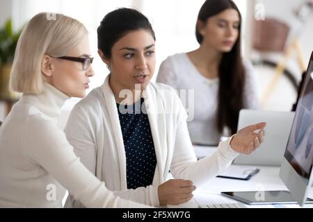 Focused multiethnic female employees cooperate on computer Stock Photo