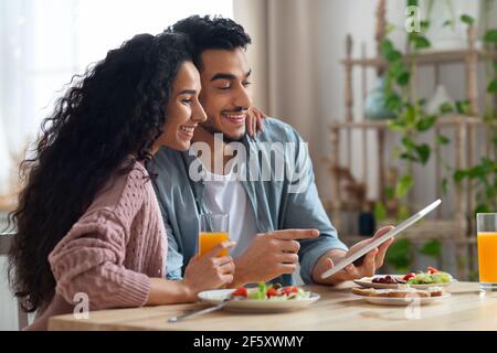 Young Arab Couple Using Digital Tablet In Kitchen While Having Breakfast Stock Photo