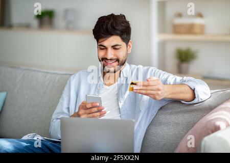 Mobile banking concept. Positive arab guy using smartphone and credit card for online shopping Stock Photo
