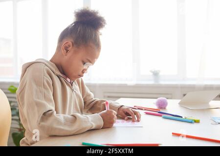 Side view view portrait of cute African-American girl signing handmade card as gift for Fathers day, copy space Stock Photo
