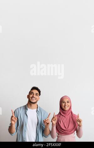 Nice Offer. Excited Muslim Couple Looking And Pointing Up At Copy Space Stock Photo