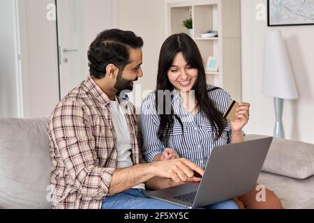 Happy indian couple shoppers doing online shopping using credit card and laptop. Stock Photo