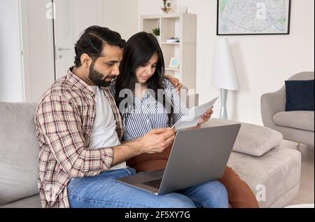 Young indian couple reading bills paying online using laptop at home. Stock Photo