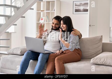Happy indian couple using laptop waving on video call virtual meeting at home. Stock Photo