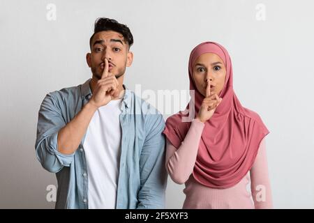 Young muslim couple making silence sign, keeping forefingers on lips Stock Photo
