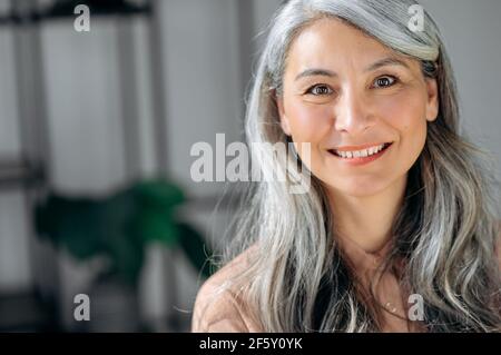 Close-up portrait of happy successful influential senior gray-haired Asian business woman, top manager, lawyer, real estate agent, standing at office, in stylish wear, looks at camera, smiles friendly Stock Photo