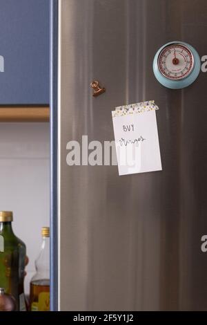 Positive sticky note pasted with a pineapples adhesive on a metallic fridge door next to a clock timer and a copper magnetic clamp in a kitchen. Stock Photo