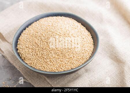 Blue ceramic bowl with raw white quinoa seeds on a gray concrete  background and linen textile. Side view, close up, selective focus. Stock Photo