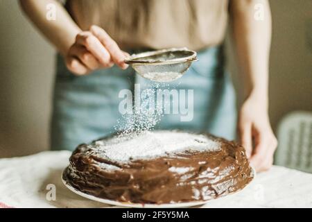 Anonymous woman pouring powdered sugar on chocolate cake Stock Photo