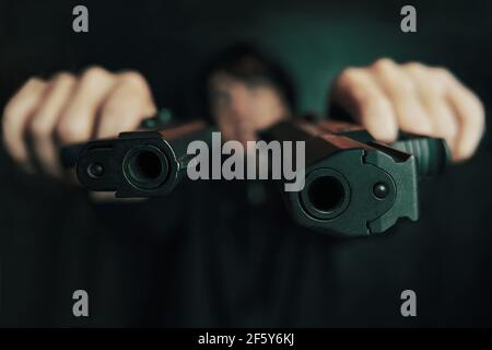 Close-up of two gun muzzles. Guy threatens with firearm. Two pistols in man's hands are pointed at camera. Criminal with weapon. Stock Photo