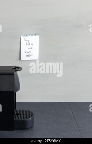 Reminder sticky note pasted with a butterflies adhesive on a gray wooden background next to a coffee machine with the sentence: Keep calm and make cof Stock Photo