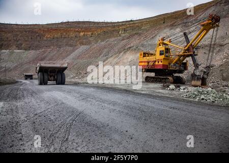 Rudny/Kazakhstan - May 14 2012:  Open-pit mining iron ore in quarry. Big yellow excavator and two  Caterpillar quarry trucks. Stock Photo