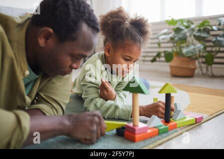 Portrait of African-American man playing with daughter while lying on floor in cozy home interior, copy space Stock Photo