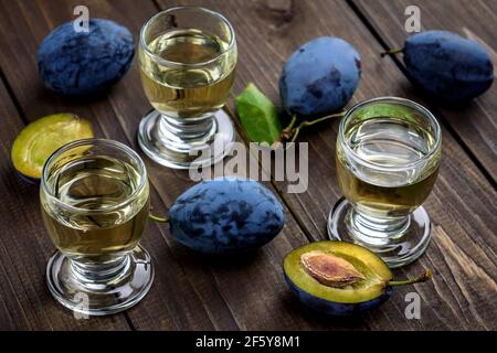 Plum brandy or schnapps in glasses and fresh tasty plums on a wooden table. Selective focus. Stock Photo