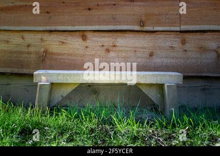 Small wooden bench on grass in front of waney edged wooden shed. Stock Photo