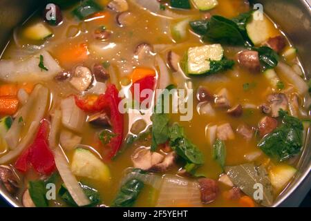 Close-up of a pot of hearty homemade vegetable soup with broth, mushrooms, carrots, spinach, zucchini, celery, onions and potatoes–chock full of goodn