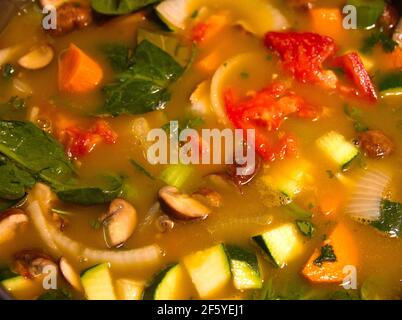 Pot of hearty homemade vegetable soup with broth, mushrooms, carrots, spinach, zucchini, celery, onions and potatoes–it's good for you.