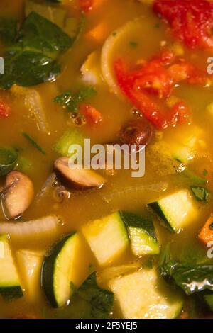 Close-up of Mom's delicious vegetable soup with broth, mushrooms, carrots, spinach, zucchini, celery, onions and potatoes–it's good for you.