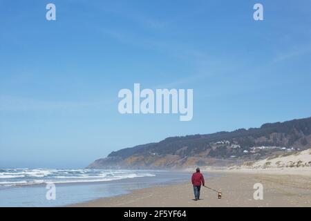 A man walking a dog on Baker Beach in Florence, Oregon, USA. Stock Photo