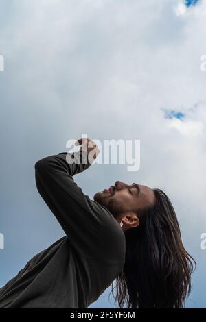 portrait of a young man on his side with arms raised. long haired young man, straight hair, relaxed in his thoughts. meditating, long haired man conne Stock Photo