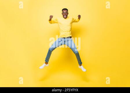 Young cheerful excited African man jumping and screaming with clenching hands on isolated yellow studio background Stock Photo