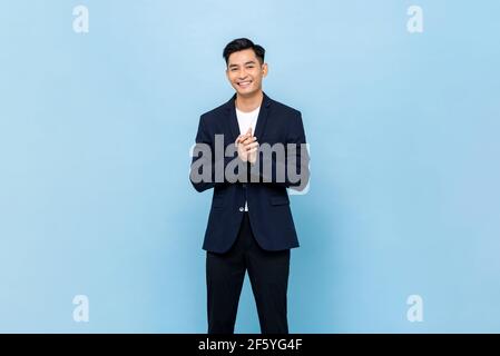 Smiling young handsome southeast Asian man clapping hands impressively in light blue studio isolated background Stock Photo