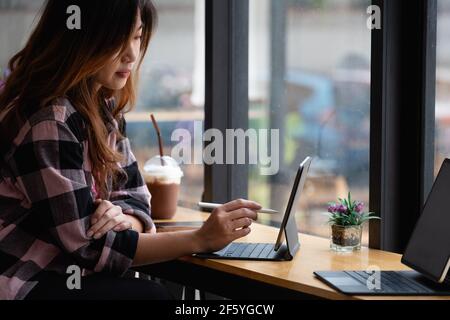Young creative designer holding stylus pen drawing on screen of digital tablet at cafe Stock Photo