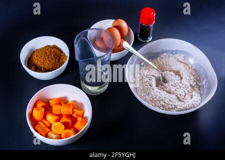 Closeup shot of bowls of ingredients for making homemade carrot muffins on a dark surface Stock Photo