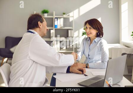Male doctor greeting handshaking smiling female patient in hospital office Stock Photo