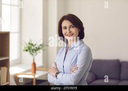 Smiling confident millennial woman standing arms crossed in home office portrait Stock Photo