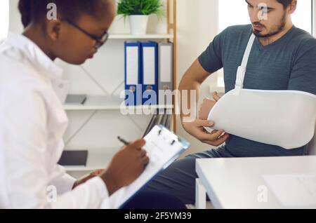 Young man with broken hand or arm in sling immobilizer seeing doctor at hospital Stock Photo