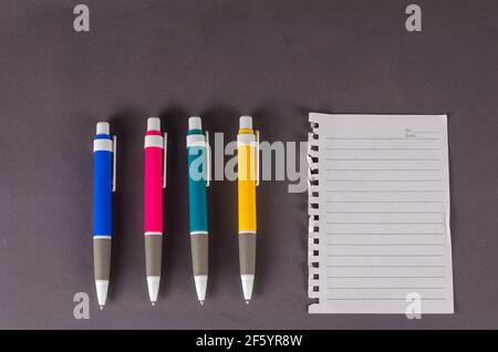 Pens and blank paper on a gray background. A set of multi-colored pens and a page torn from a notebook. Top view, flat lay Stock Photo