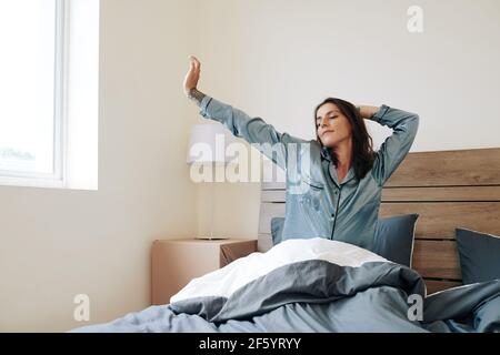 Beautiful young woman in silk pajamas stretching in bed after waking up in the morning Stock Photo