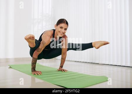 Smiling strong young woman standing on hands, raising legs and looking at camera Stock Photo