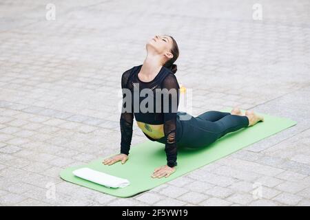Fit young woman practicing yoga outdoors and doing cobra pose that helps to open chest and shoulders Stock Photo